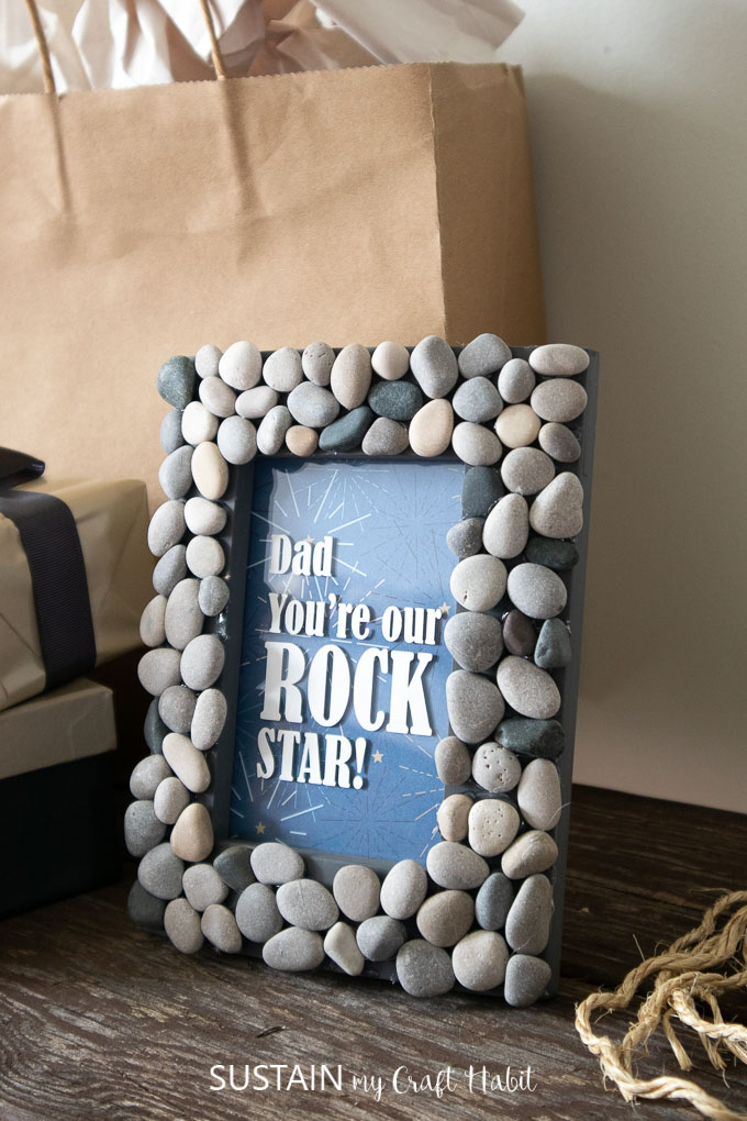 A picture frame with rocks glued around the frame and text on the glass saying "Dad you're our rock star!"