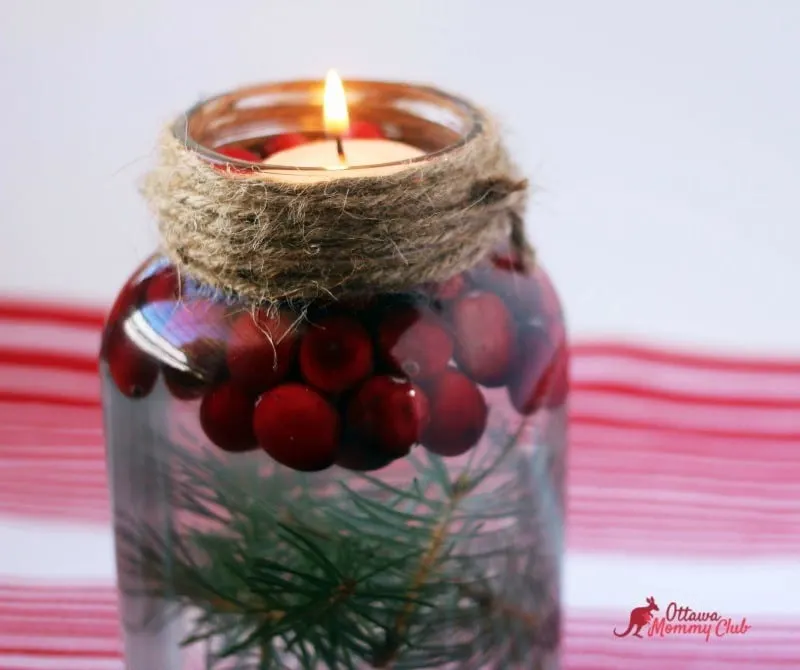 A mason jar candle with tree trimmings and cranberry lit up.