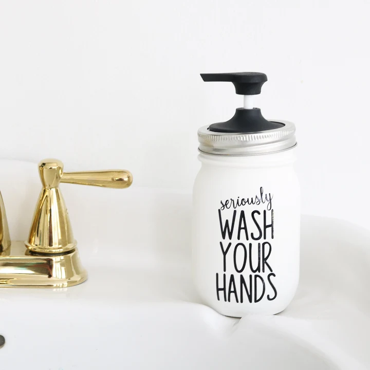 A white painted mason jar with a black soap pump on top. The saying wash your hands is applied to the surface of the jar.