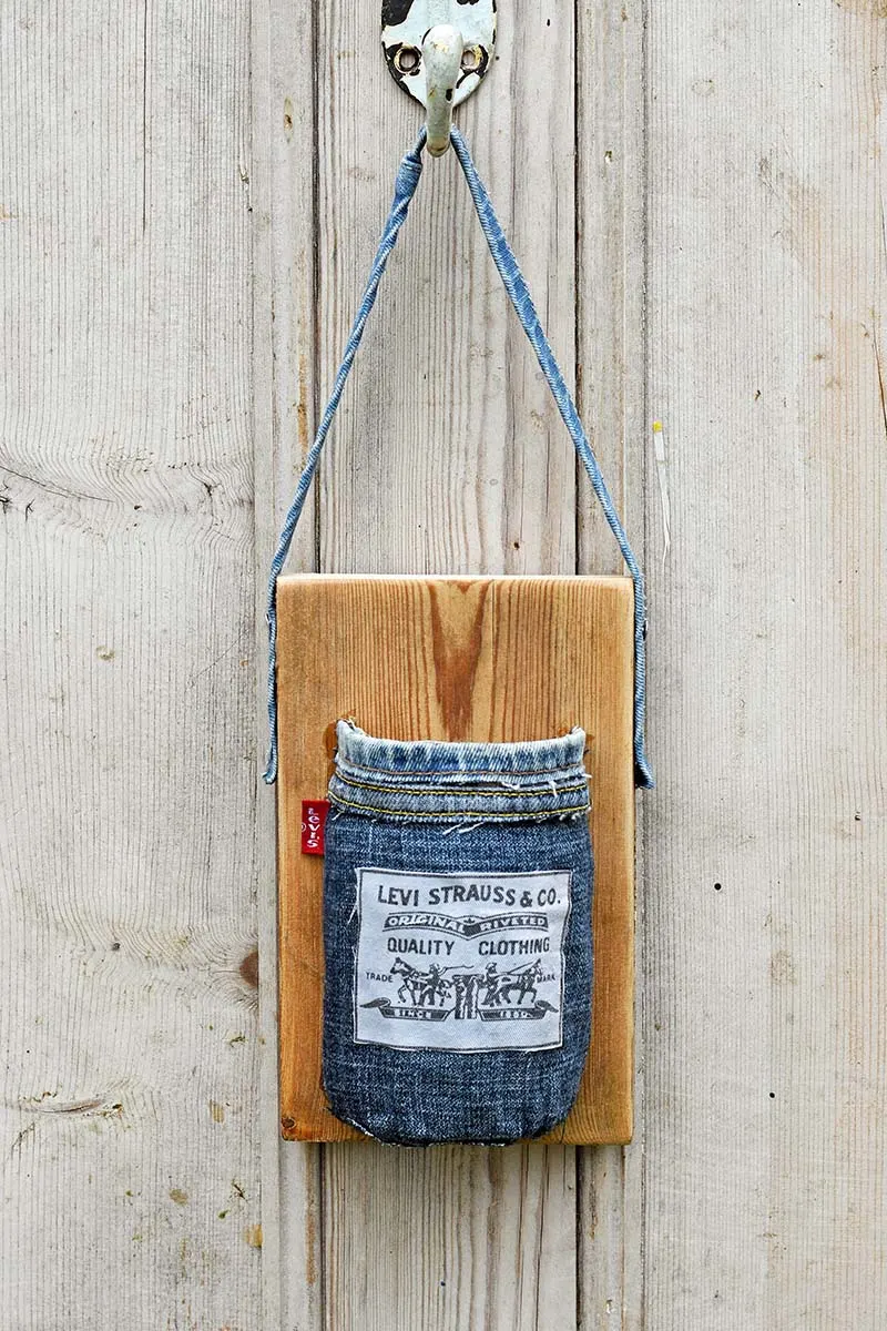 A mason jar wrapped in denim and attached to wood board.