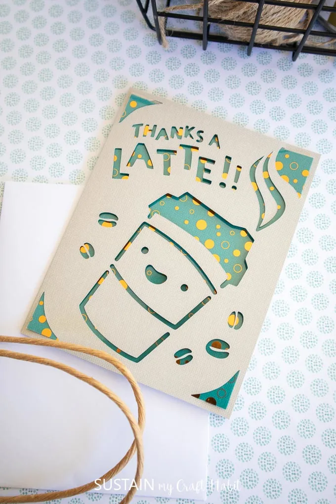 A greeting card with a coffee cup and coffee beans cutout from the front, and letter cut outs spelling "thanks a latte"