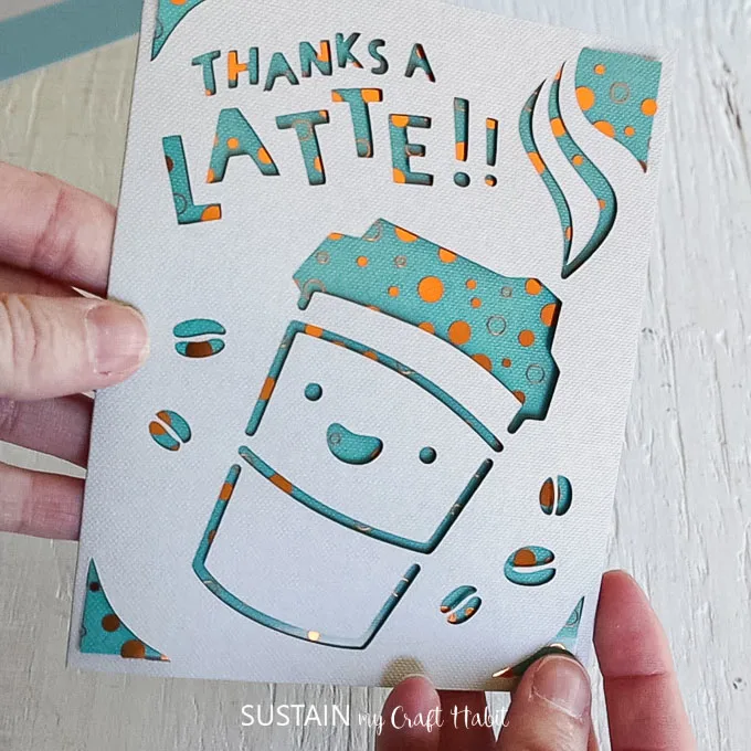 Finished card with a coffee cup and coffee beans cutout from the front, and letter cut outs spelling "thanks a latte."