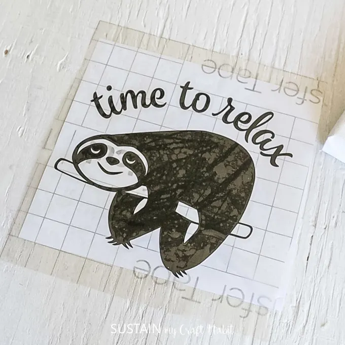Placing a piece of transfer tape over top of the sloth vinyl image.