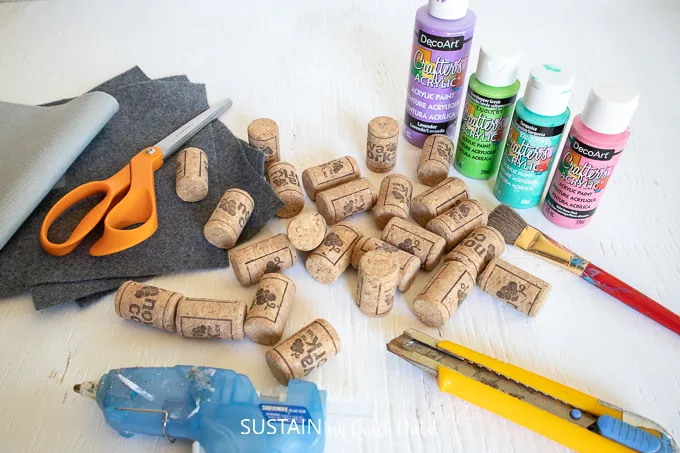 Materials needed to make a colorful DIY wine cork coasters including wine corks, scissors, hot glue, felt fabric, paint brush and paint.