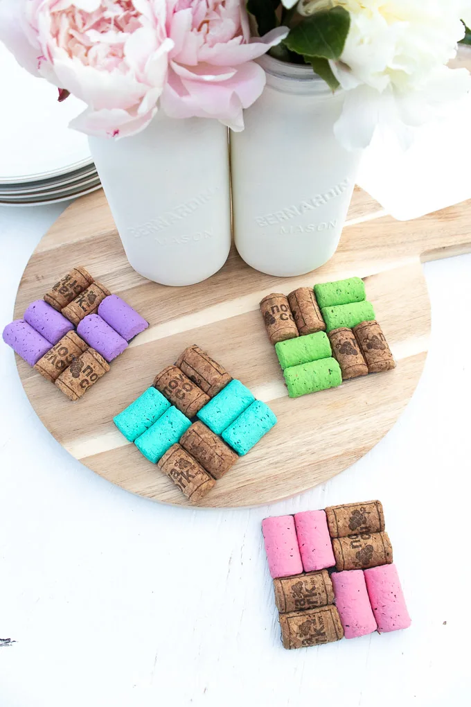 Finished colorful DIY Wine Cork Coasters set on a table and tray next to a vase with flowers.