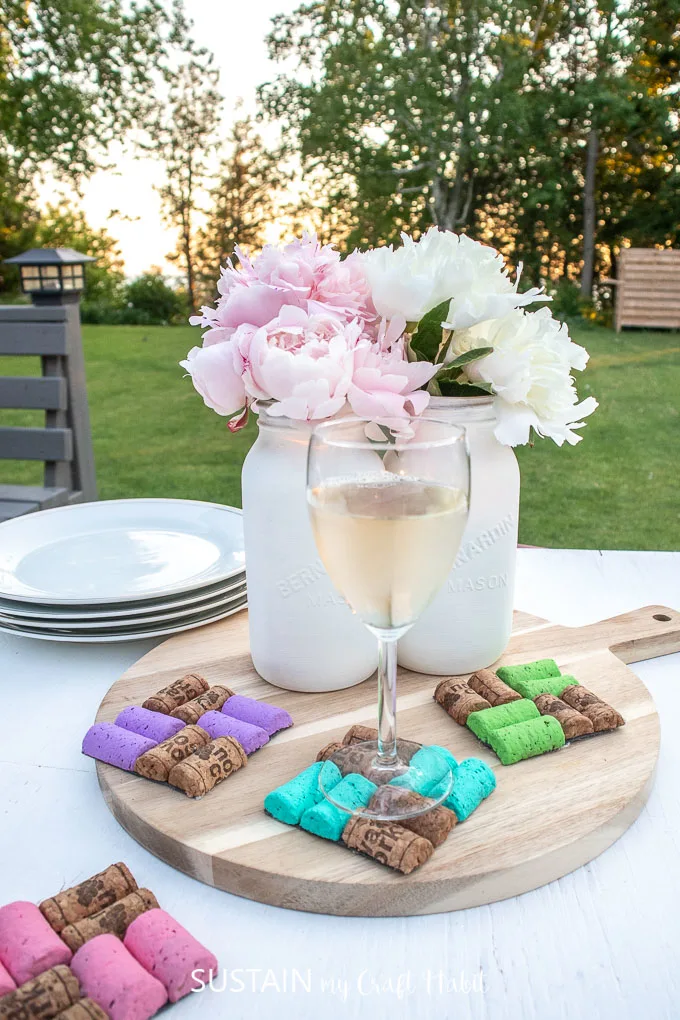 Colorful DIY Wine Cork Coasters set on a table and tray with a wine glass, vases, flowers and plates.