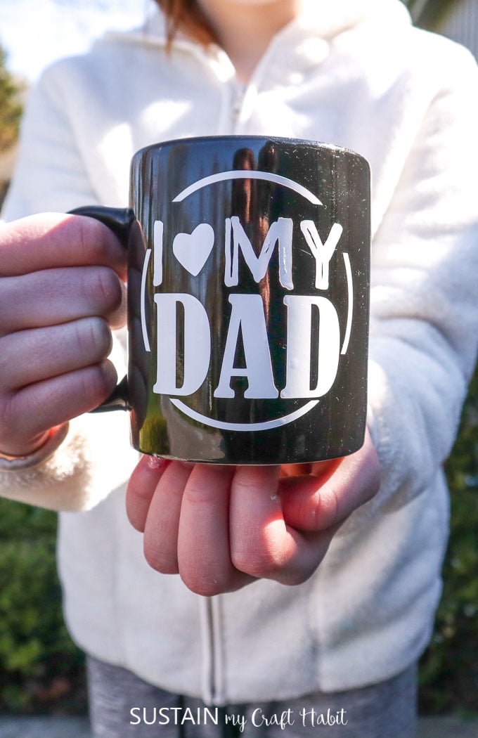 Holding a black mug with "I heart my Dad" written on the front.