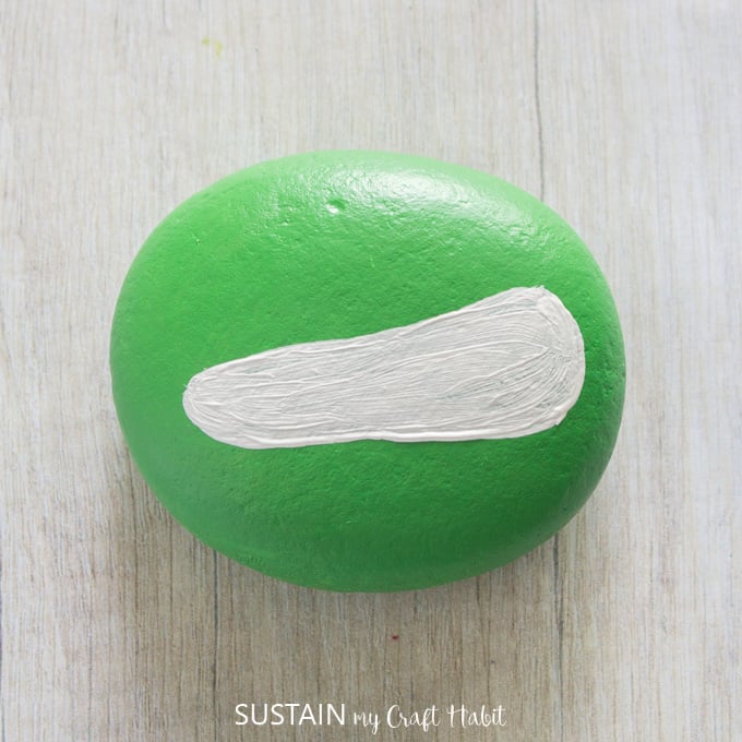 Painting a white oval on the green painted rock.