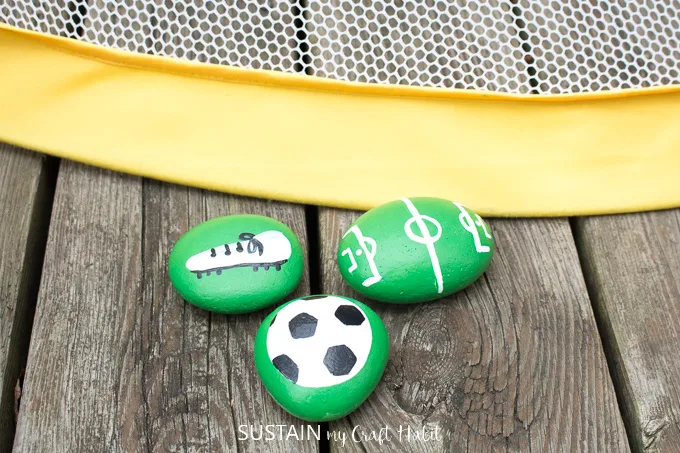 Painted soccer rocks with a image of a soccer ball, cleats and soccer pitch.