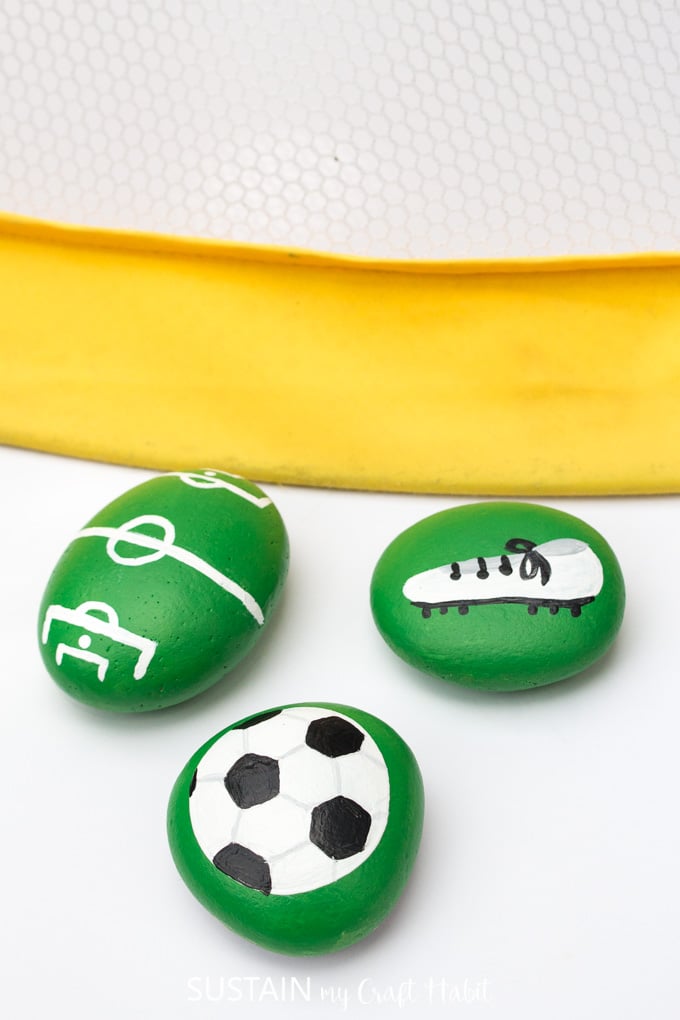 Painted soccer rocks with a image of a soccer ball, cleats and soccer pitch.