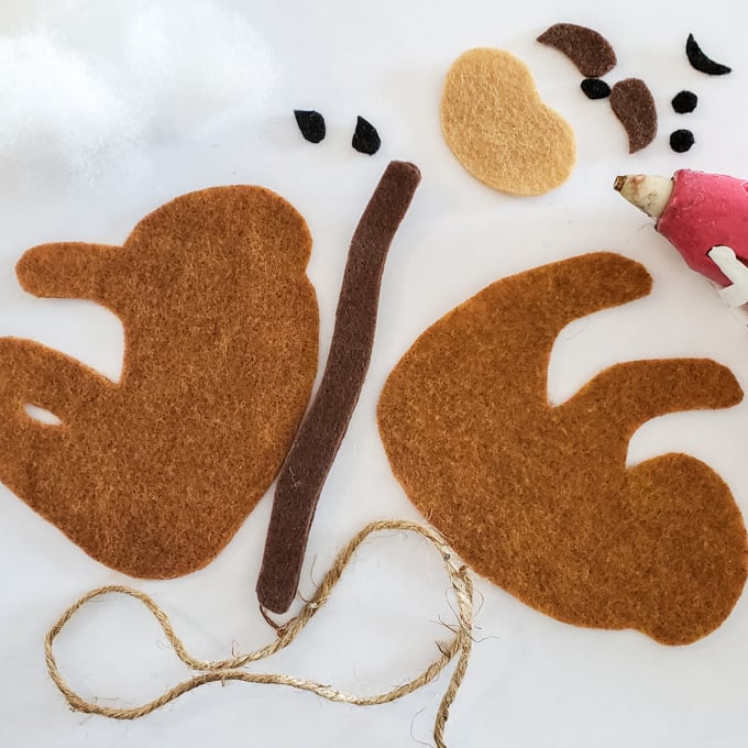 Materials needed to make no-sew sloth ornaments including felt fabric, twine, tweezers and a hot glue gun.