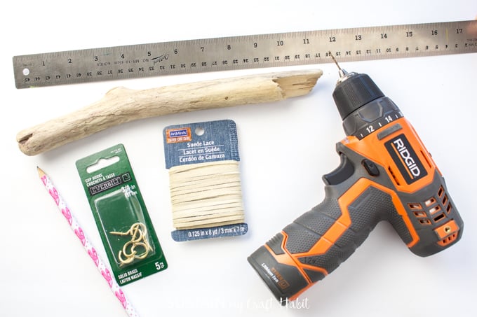 Materials needed to make a boho driftwood jewelry organizer, including driftwood, gold hooks, a drill, pencil and wood glue.