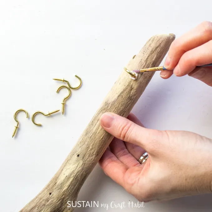 Placing the gold hook in the driftwood and using a brush to remove excess glue.
