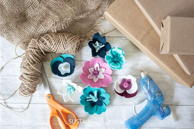 Materials needed to for a creative gift wrapping idea including kraft paper, burlap and felt flowers.