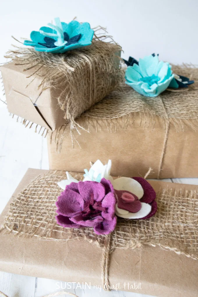 Gifts wrapped with brown paper, burlap and twine with the top adorned with felt flowers.