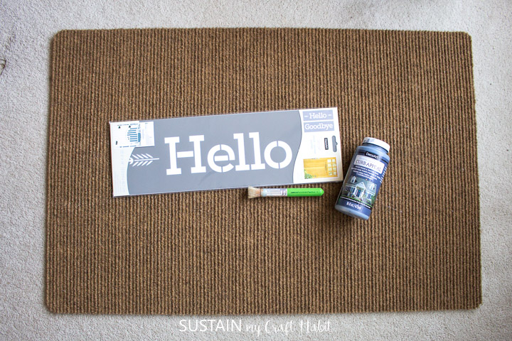 Materials needed to paint a welcome mat including a mat, stencil, paint and a paintbrush.