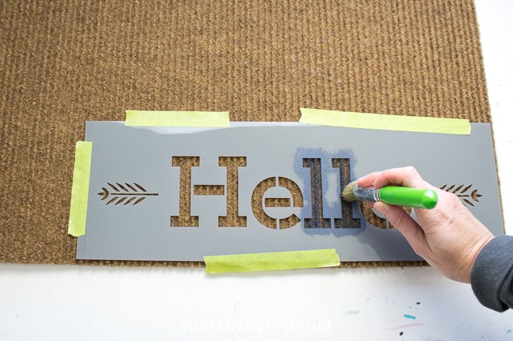 Using a stencil brush to dab paint over the "hello" stencil.