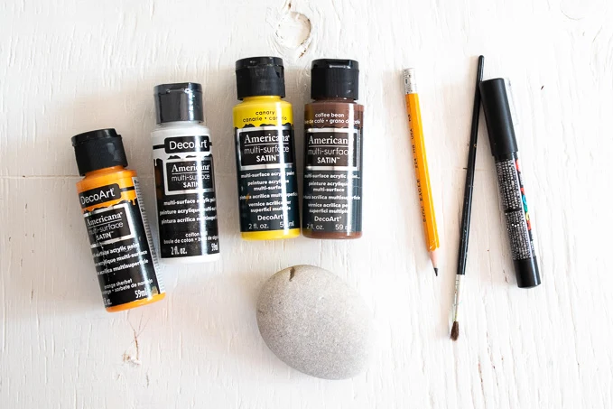 Supplies needed to paint sunflower rocks including stone, paints, pencil, brush and paint pen.