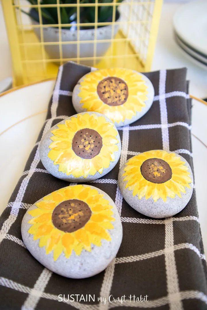Pretty sunflower painted rocks on top of a dinner plate setting.