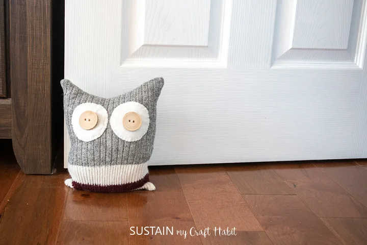 Upcycled sock owl door stop placed in front of a door to hold it open.