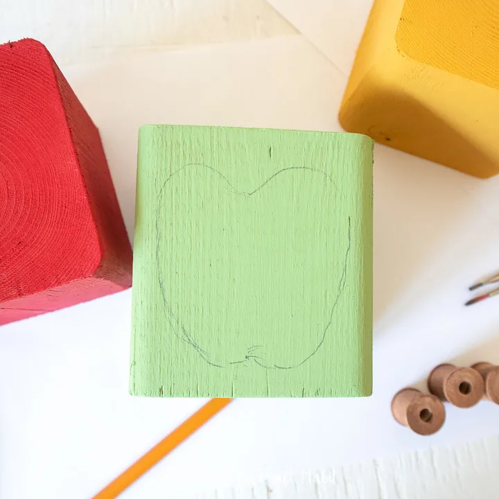 Drawing the outline of an apple on the green painted wood block.