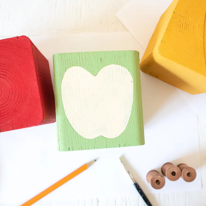 Painting a  half apple on a green wooden block.