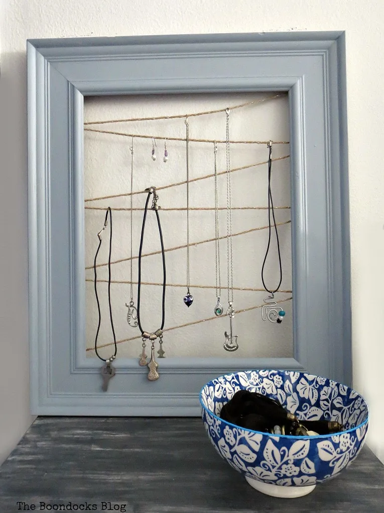 A gray wood frame strung with zig zagging twine upon which necklaces and earrings hang.