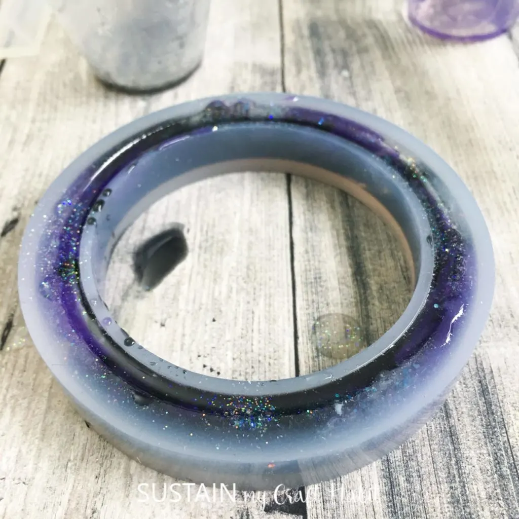 Filling the silicone bracelet mold with resin and adding glitter.