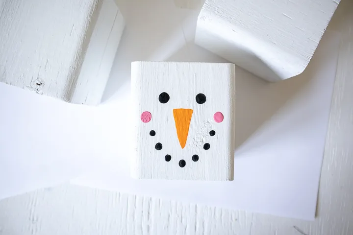 Adding pink paint to the wooden block to look like snowman cheeks.