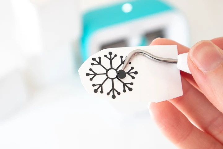 Using a weeding tool to remove excess vinyl from the snowflake cut image.