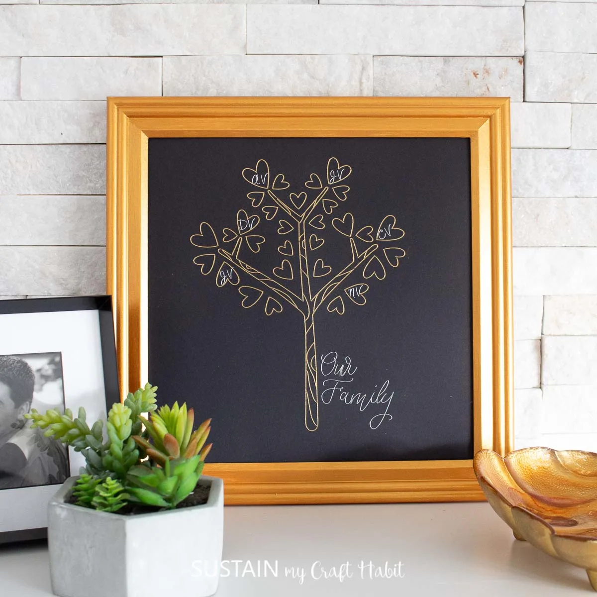 Framed family tree craft resting on a white surface, leaning against a white brick background.