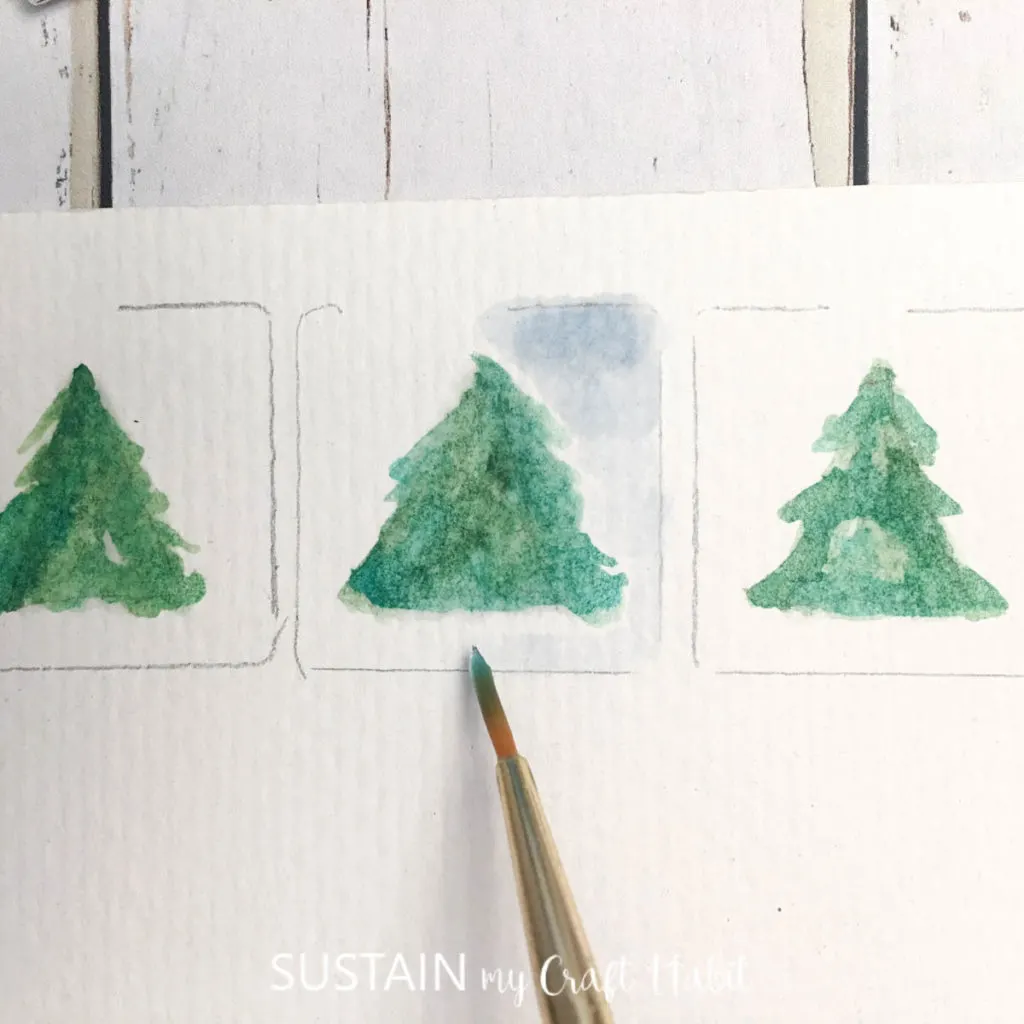 Painting a blue background around the green tree.