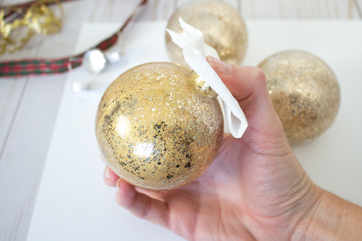 Covering the opening of the glass ornament and shaking the gold paint inside until it is mixed together.