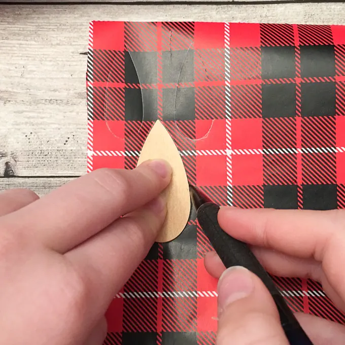 Tracing the wood shape onto the plaid gift wrap paper.