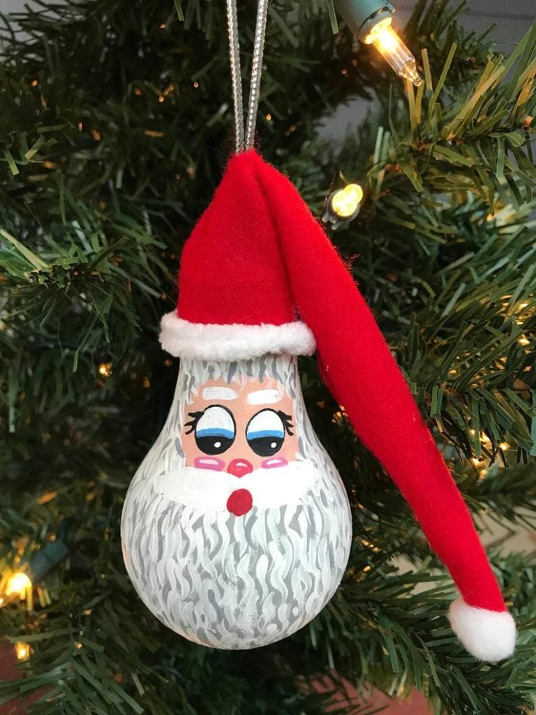 Santa light bulb ornament on a tree.