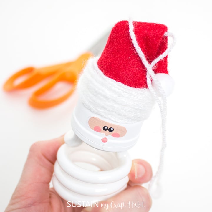 Tying the yarn into a knot on the light bulb Santa Claus ornament.