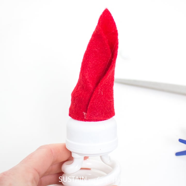 Gluing the felt fabric together to make a Santa Claus hat on the top of the light bulb.