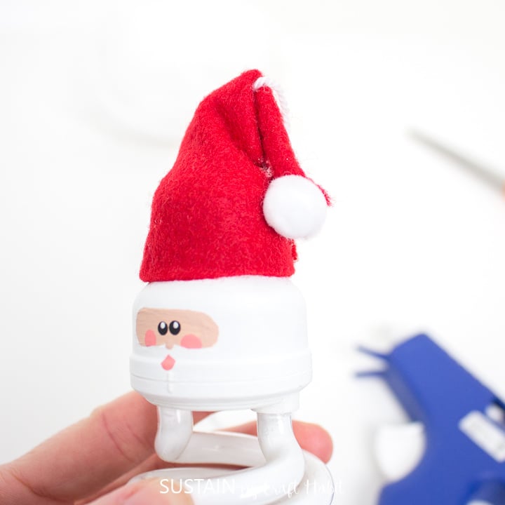 Gluing a pom pom to the top of the felt Santa Claus hat.
