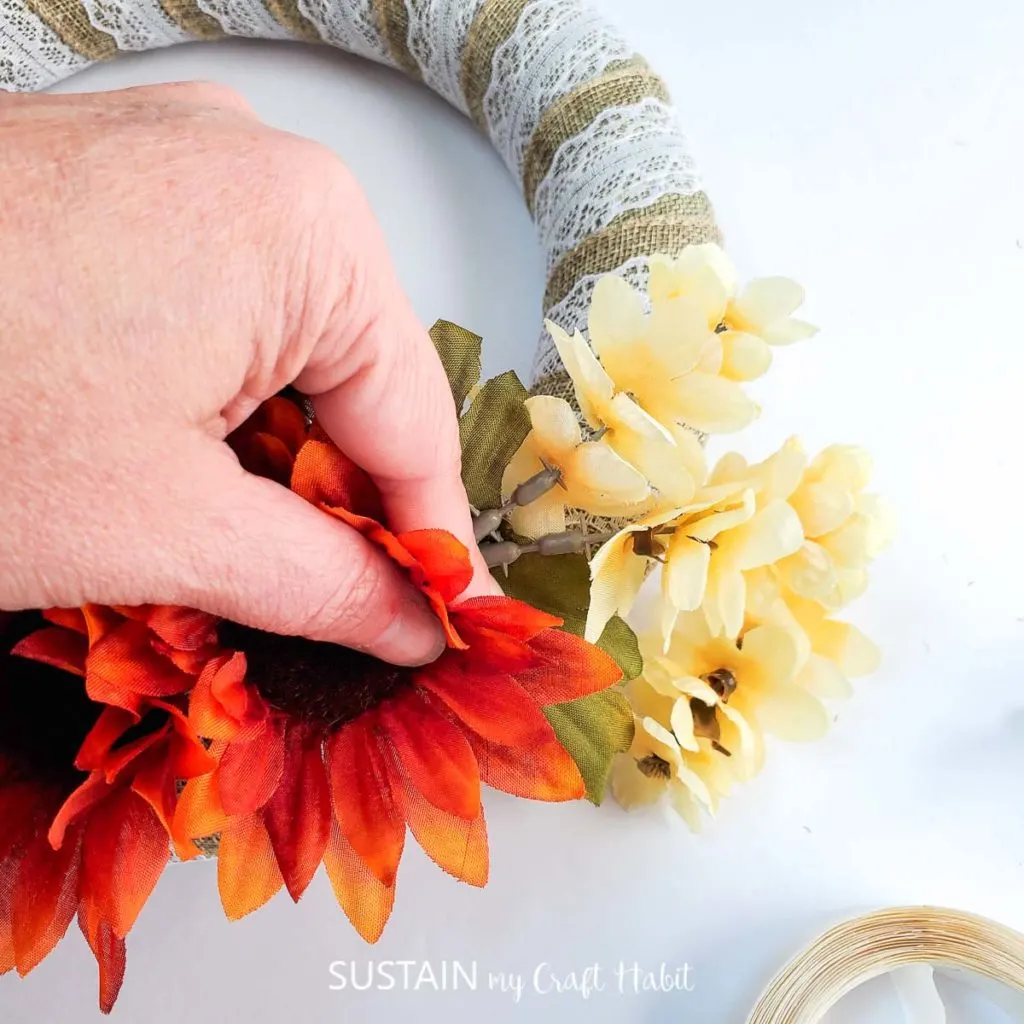 Attaching the plastic sunflower and cream flower onto the foam wreath.