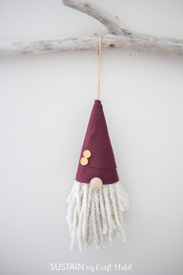 Finished gnome Christmas ornament with burgandy hat, hanging from a tree branch.