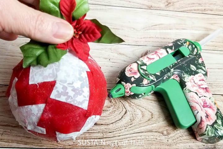 Hot gluing a Christmas holly onto the scrap fabric decoupaged ornament.