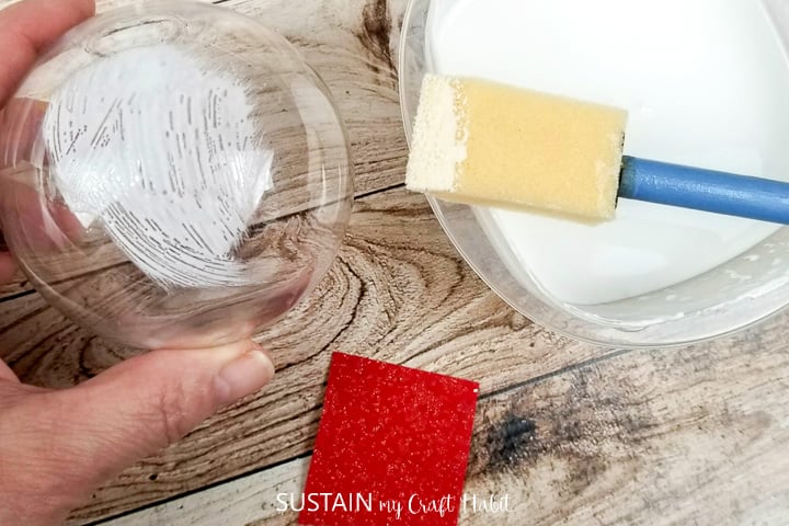 Applying mod podge to a glass ornament.