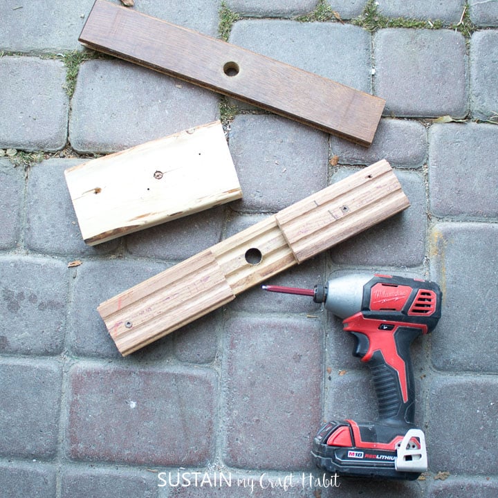 Using a drill to screw in small wooden boards to the bottom of the long board.