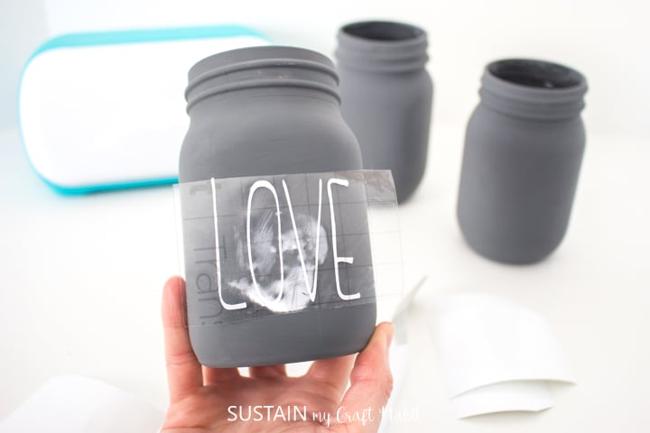 Positioning the cut phrase and vinyl tape on the chalky painted mason jar.