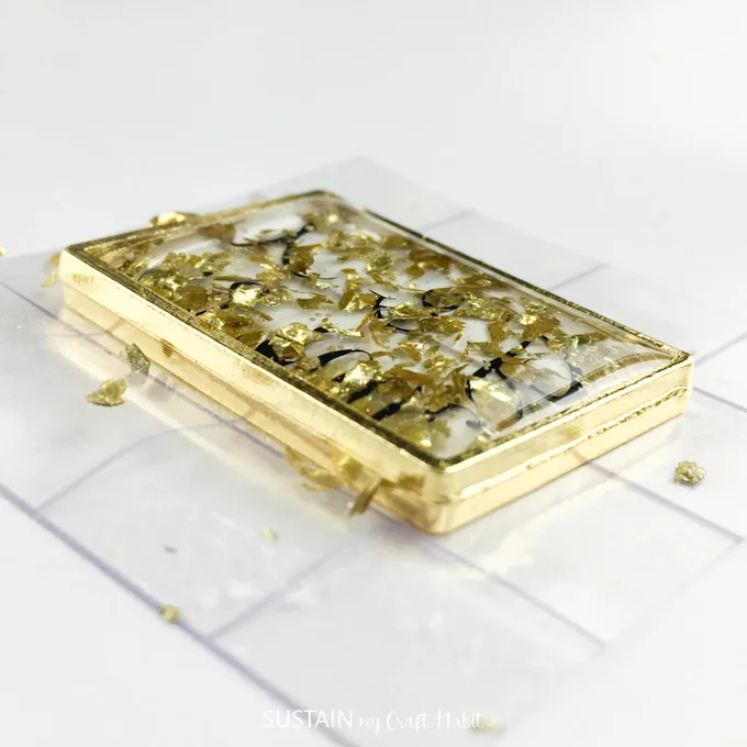 Bezel poured with resin with gold flakes laid on a wood background. 