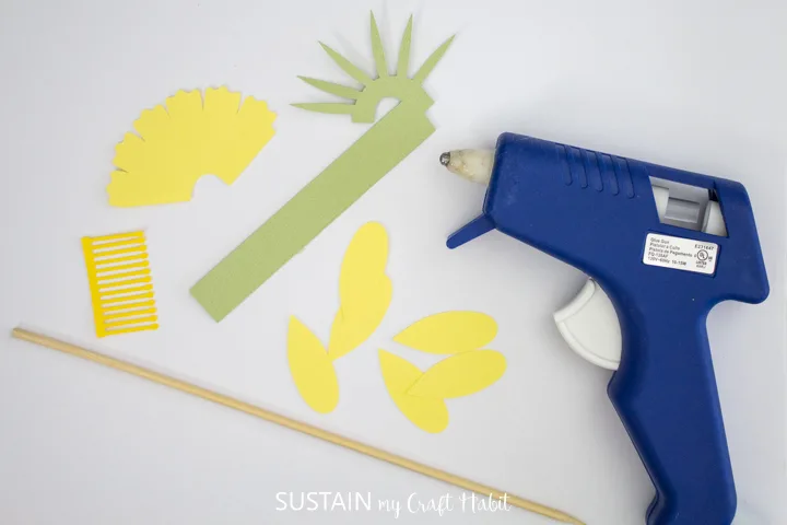 Materials needed to make daffodil paper flowers including a wooden dowel, hot glue gun and cut paper.