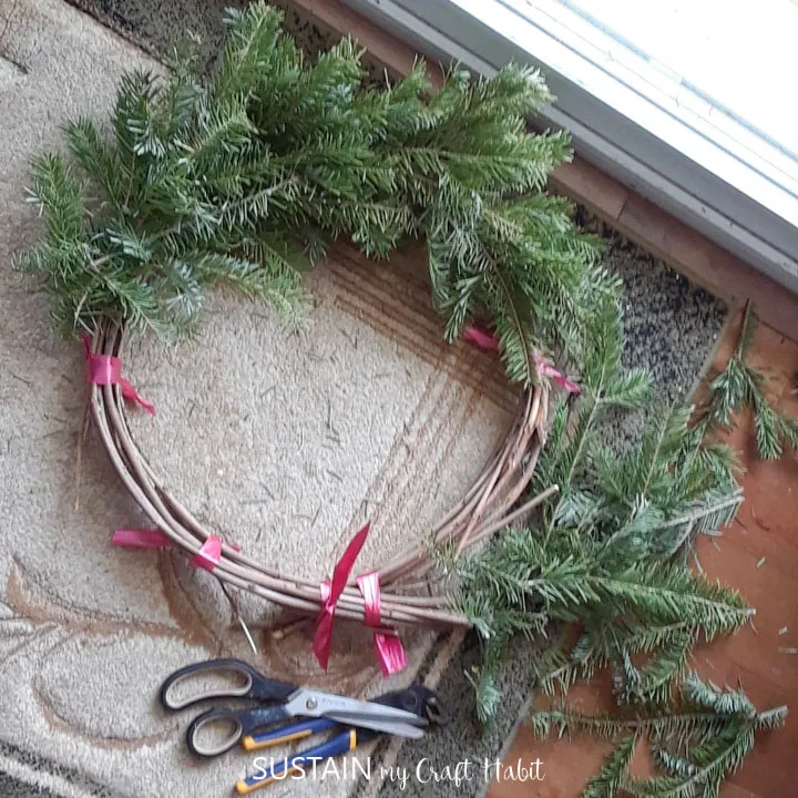 Securing pieces of evergreen trimmings on a grapevine wreath.