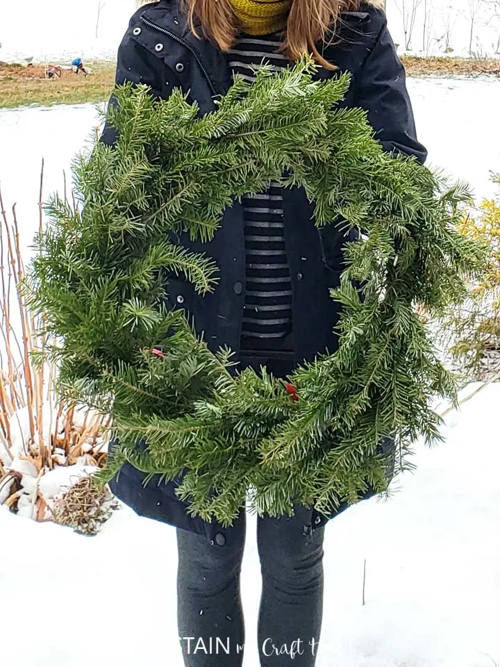 Woman holding a finished evergreen wreath.