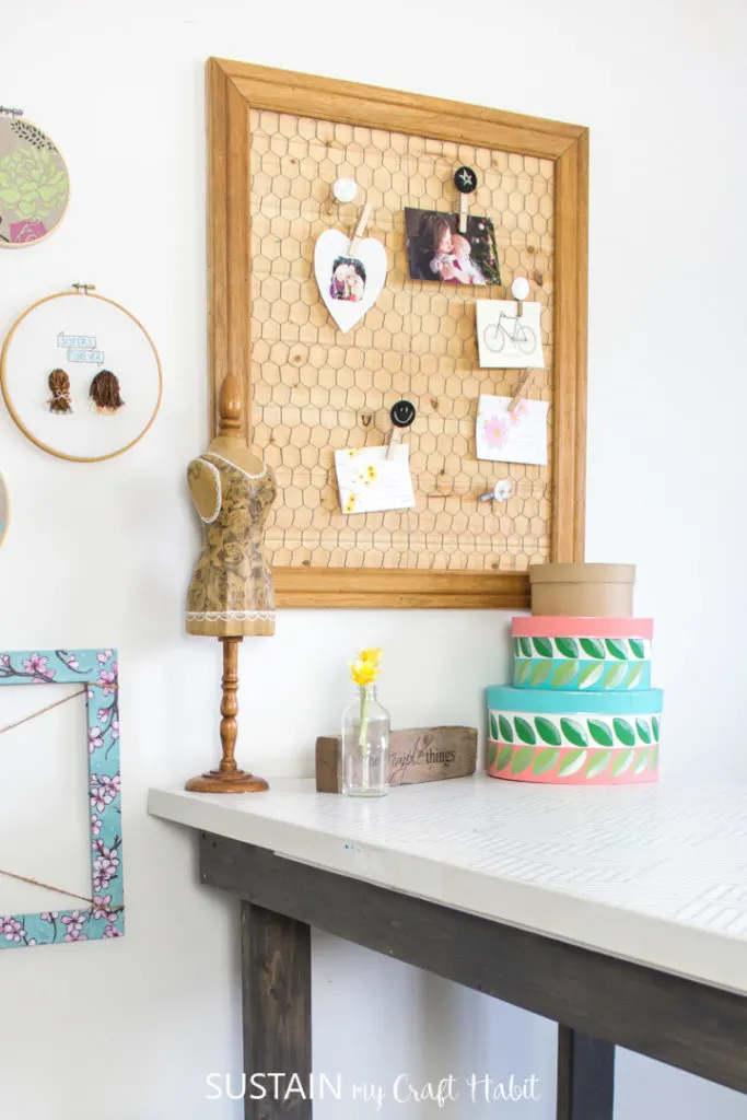 Memo board made with wood and chicken wire hanging on a wall above a work table.