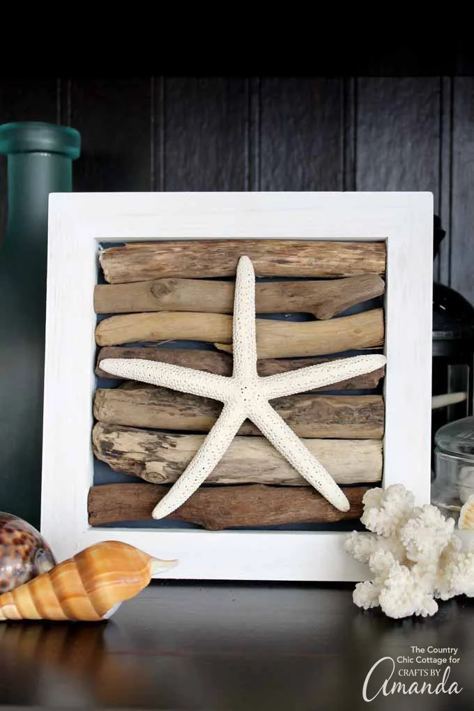 A small framed piece of coastal decor with pieces of driftwood arranged behind a starfish.
